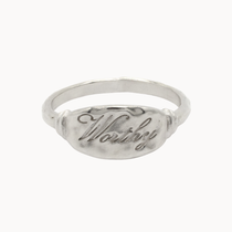 A silver signet ring with a textured oval face featuring the engraved script word 'Worthy', shown on a plain white background.