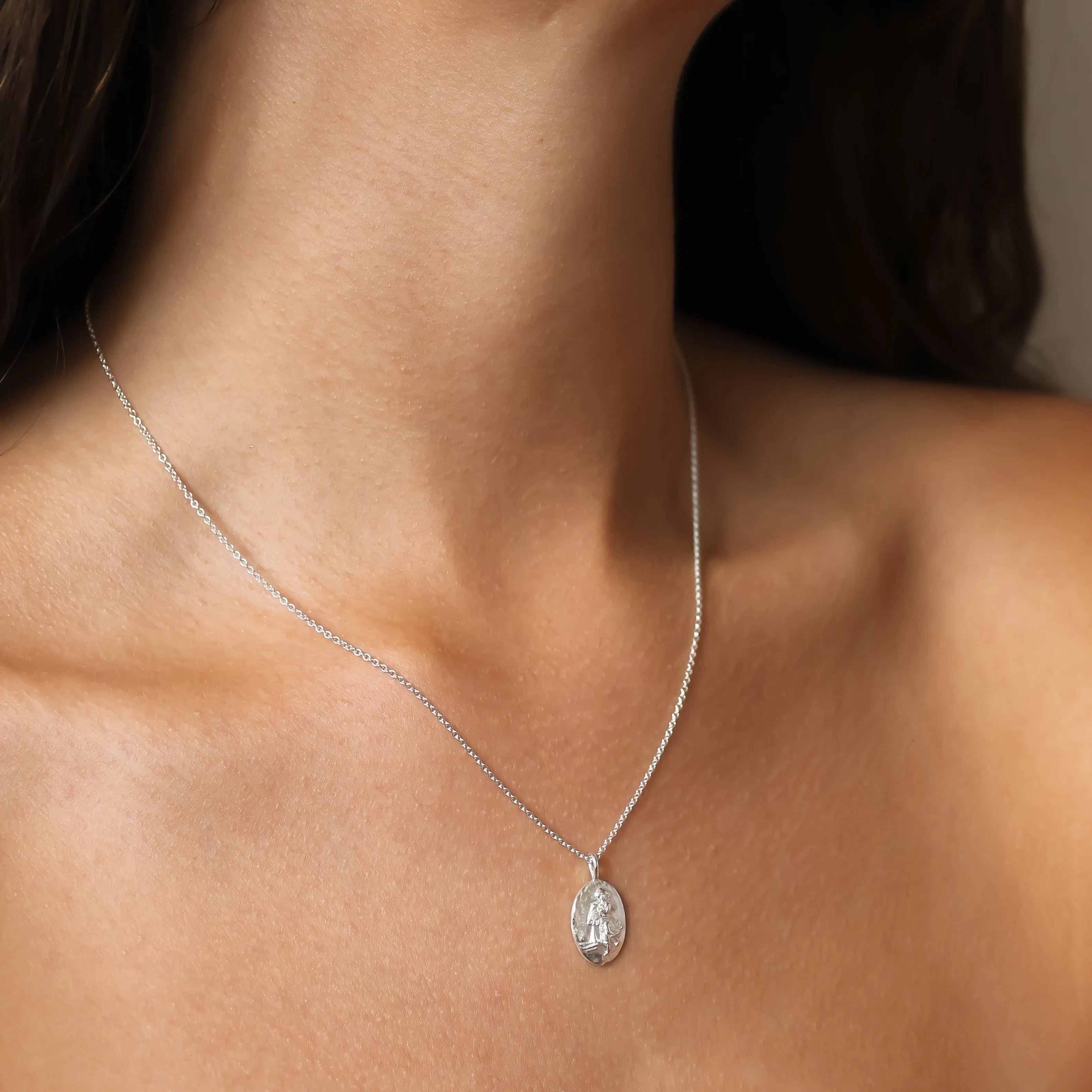 close up of neck wearing a silver aquarius star sign necklace with oval pendant and embossed detailing
