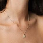 A delicate gold chain necklace with a small oval pendant featuring an embossed Aquarius star sign design, shown worn on a model's neck.