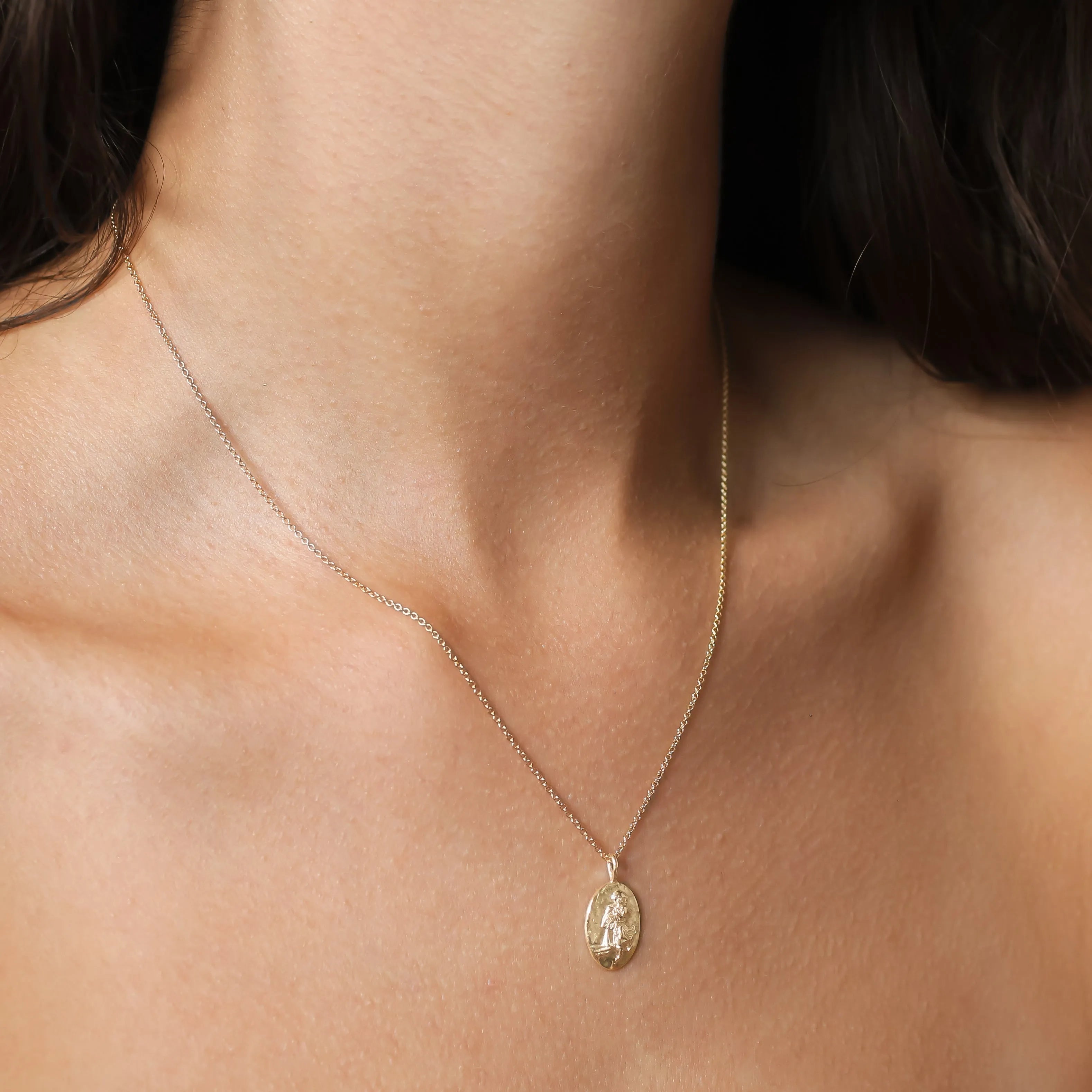 A delicate gold chain necklace with a small oval pendant featuring an embossed Aquarius star sign design, shown worn on a model's neck.