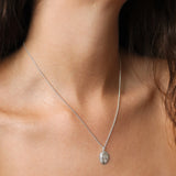 A close-up of a delicate silver chain necklace with an oval pendant featuring an engraved Aries zodiac design, worn on a model's neck.