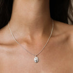 A close-up of a delicate silver chain necklace with an oval pendant featuring an embossed Cancer crab design, worn on a model's neck.