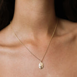 A delicate gold chain necklace with an oval pendant featuring a raised Cancer crab design on its face, worn on a model's neck.
