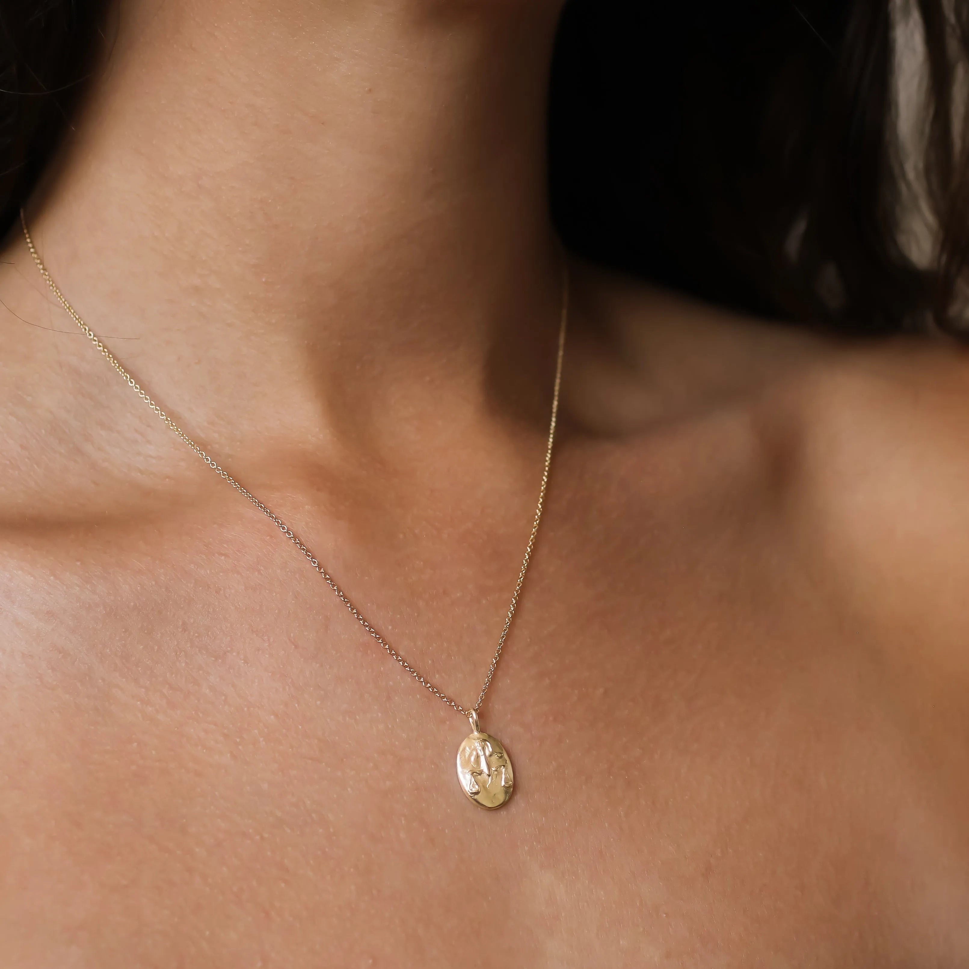 A delicate gold chain necklace with a small oval pendant featuring an engraved Libra zodiac design, shown worn on a model's neck.