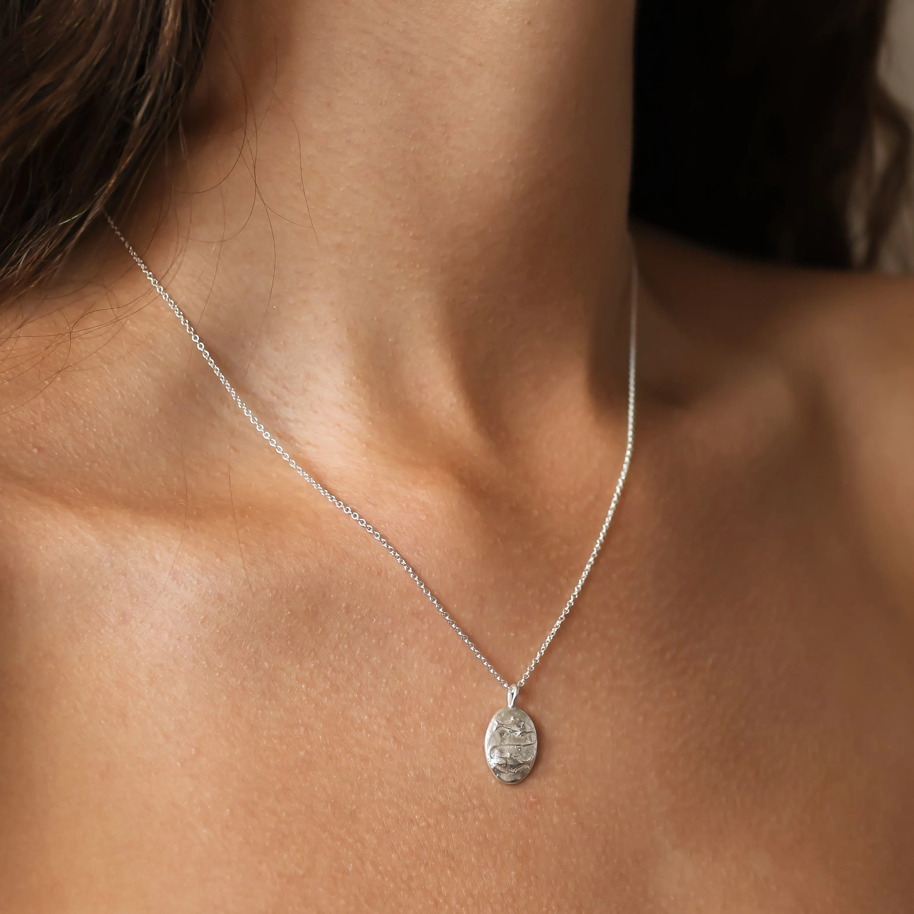 close up of neck wearing silver pisces necklace with oval embossed pendant with fish symbol