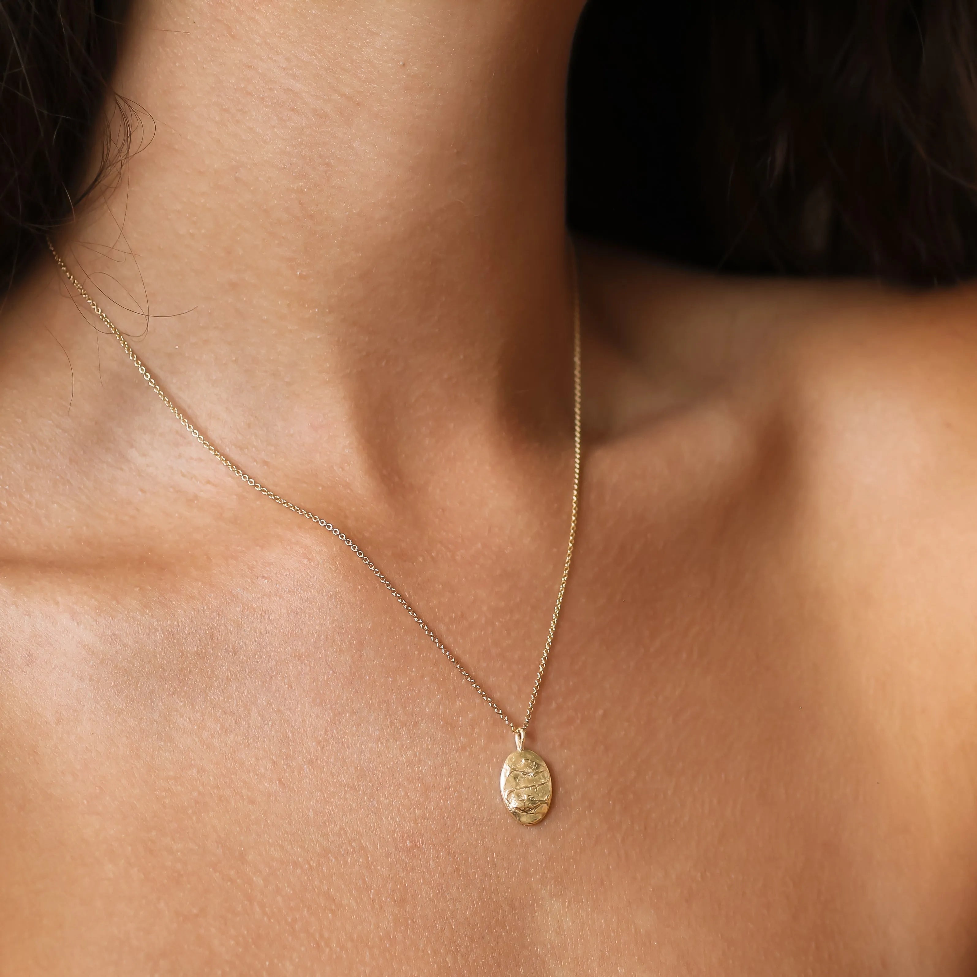 A delicate gold chain Pisces necklace with a small oval pendant worn on a model's neck, shown in a close-up shot.