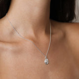 A close-up of a delicate silver chain scorpio necklace with a small, textured oval pendant worn on a model's neck.