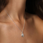 A close-up of a delicate silver chain necklace with an oval textured Taurus pendant worn on a model's neck.