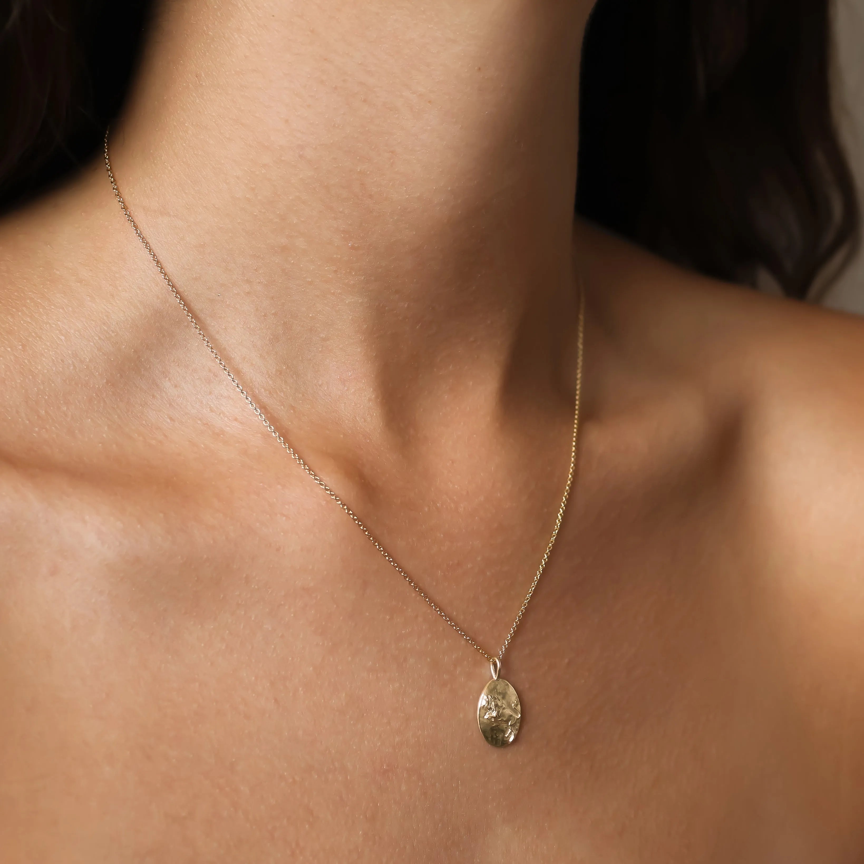 A delicate gold Taurus necklace with a small, textured gold oval pendant, shown worn on a model's neck.