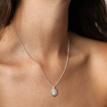 A close-up of a delicate silver chain star sign necklace with an oval pendant featuring a detailed Virgo design, worn on a model's neck.