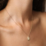A delicate gold chain Virgo necklace with an oval pendant worn on a model's neck, shown in a close-up shot.