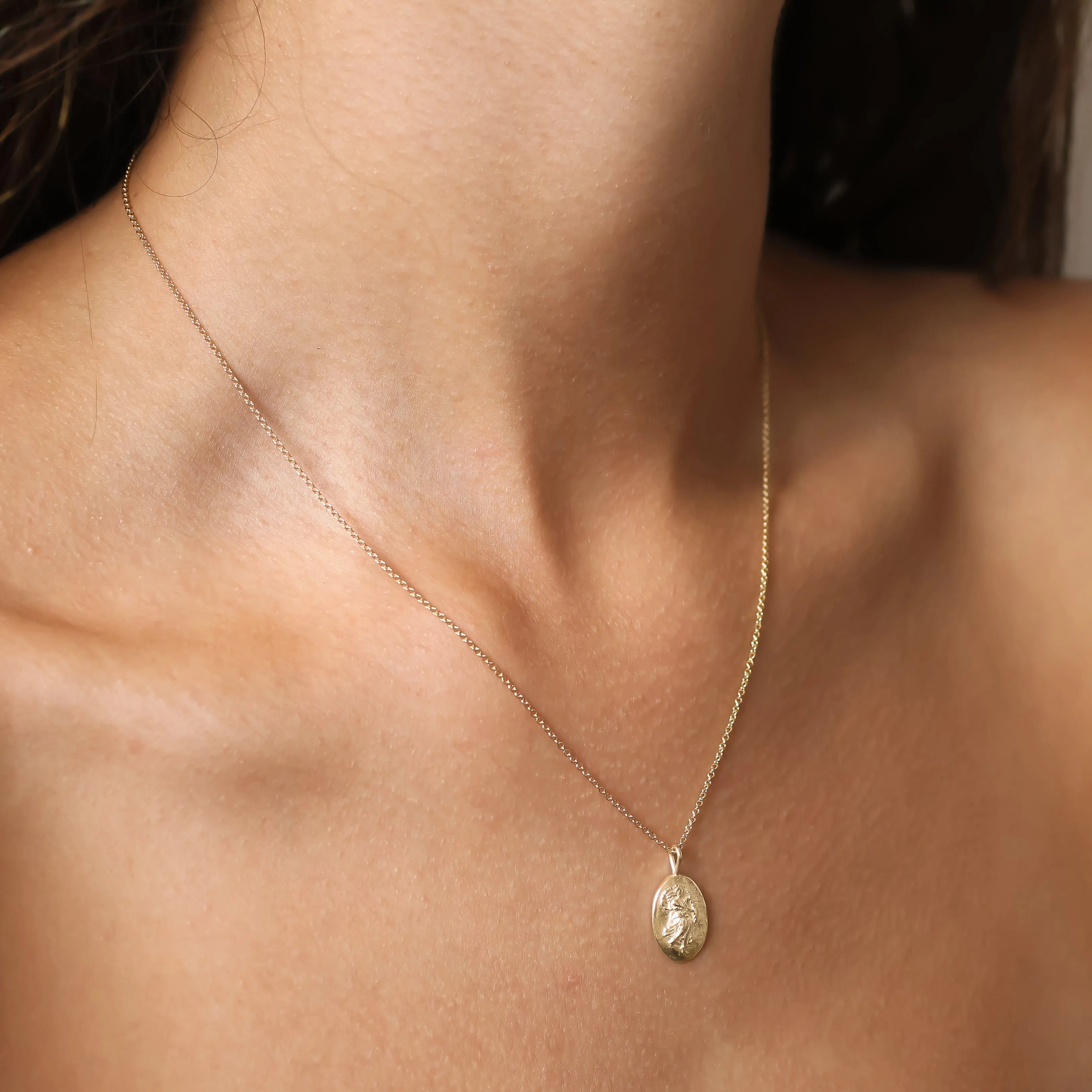 A delicate gold chain Virgo necklace with an oval pendant worn on a model's neck, shown in a close-up shot.