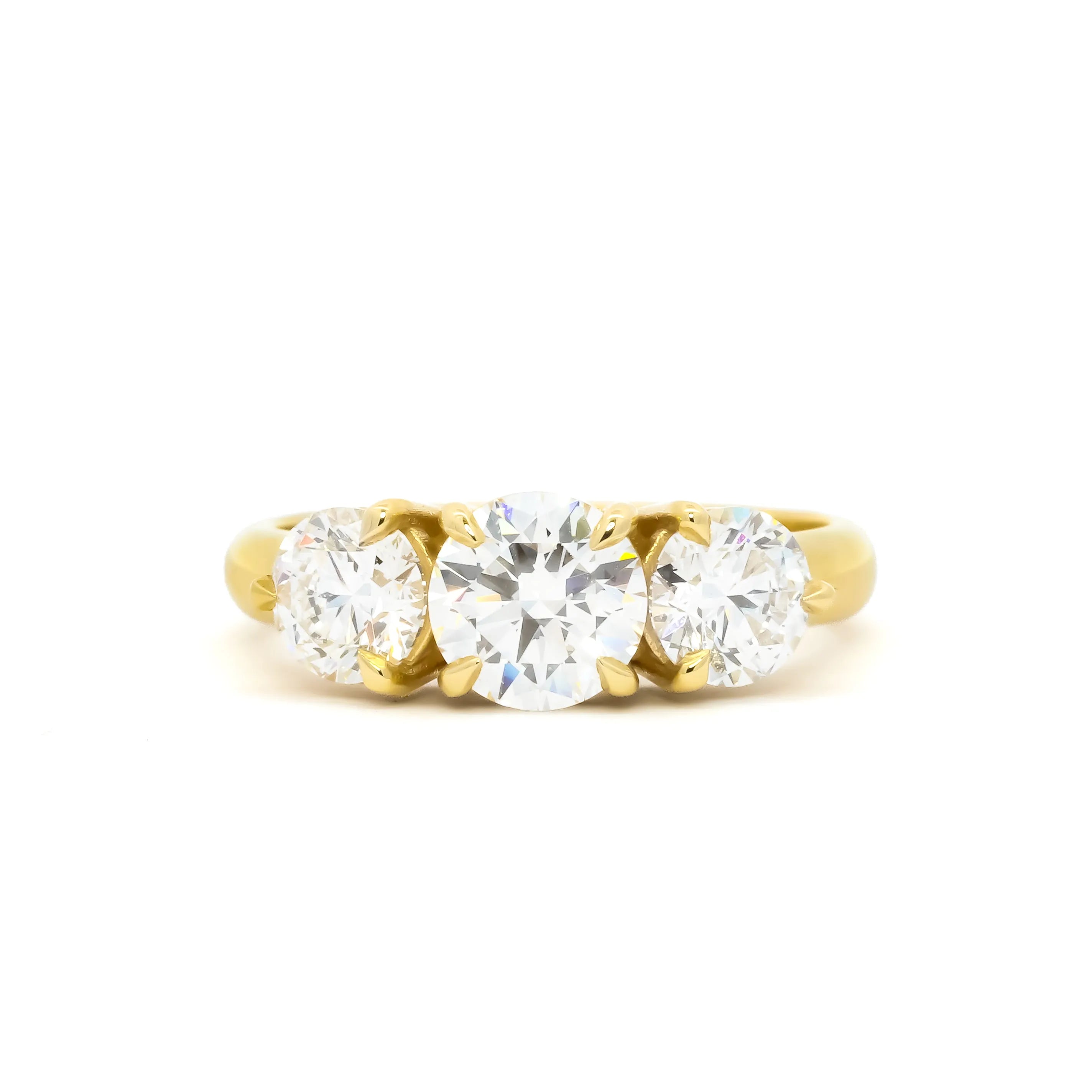 A yellow gold three-stone ring featuring a large round center diamond flanked by two smaller round diamonds, set in a classic prong setting against a plain white background.