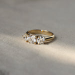 A yellow gold three-stone diamond ring resting on a textured beige fabric surface under soft, natural light.