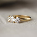 A yellow gold three-stone ring with round-cut clear gemstones, resting on a soft beige fabric surface.