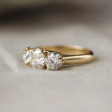 A yellow gold three-stone ring with round-cut clear gemstones, resting on a soft beige fabric surface.