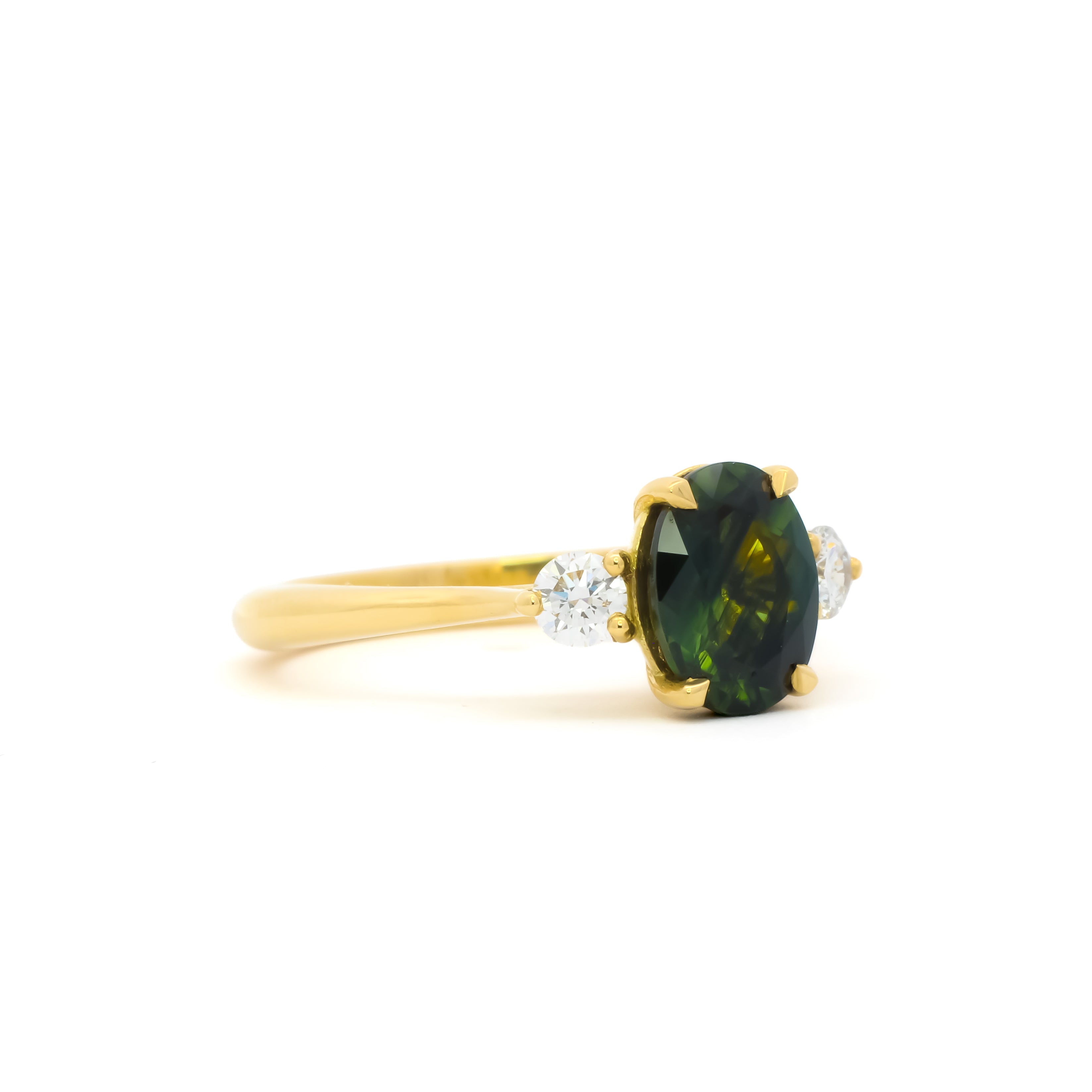 side view of a three stone engagement ring with green oval sapphire and round diamonds against a white background