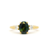 A yellow gold ring featuring an oval dark green sapphire in the center, flanked by two small round diamonds on either side of the band, set against a plain white background.