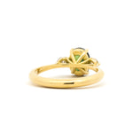 back view of a high-set green oval trilogy engagement ring in yellow gold on a white surface