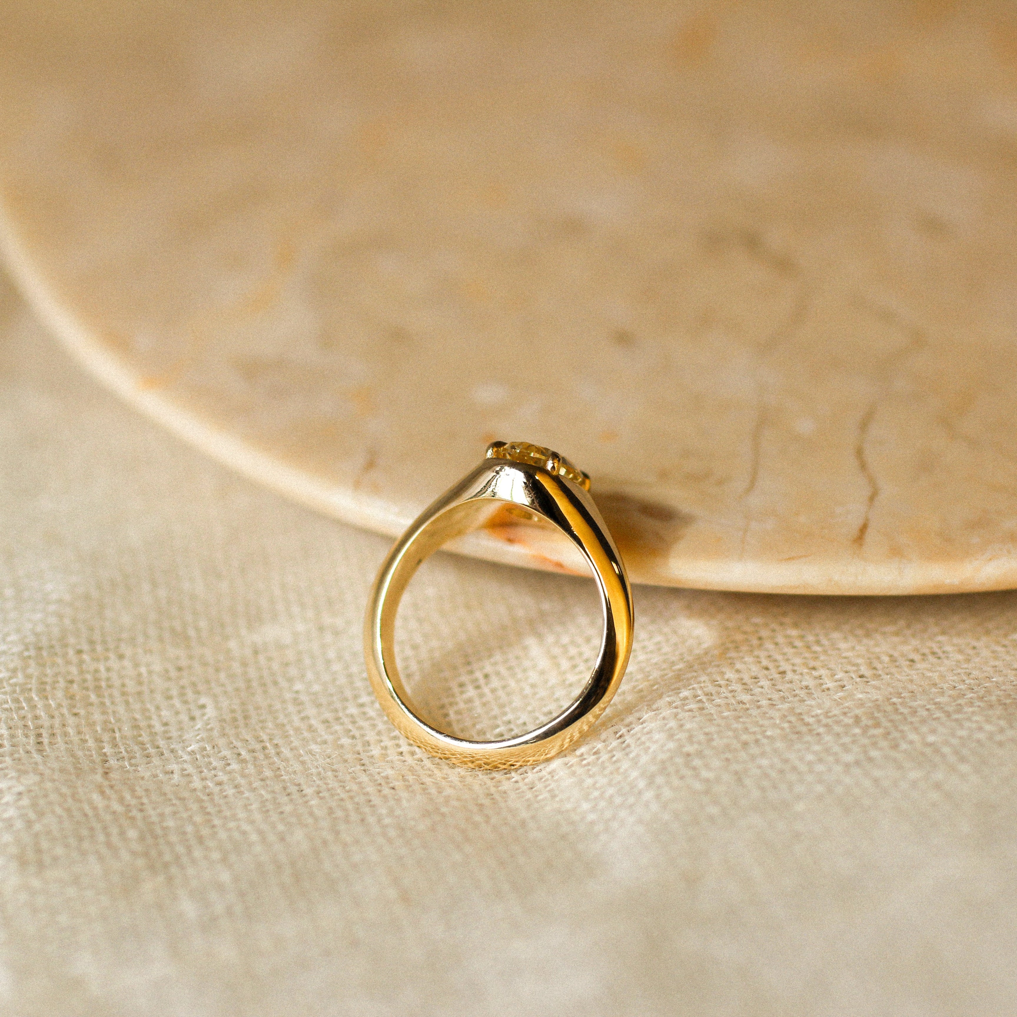 side view of a yellow diamond engagement ring with claws resting against a marbled ceramic tray