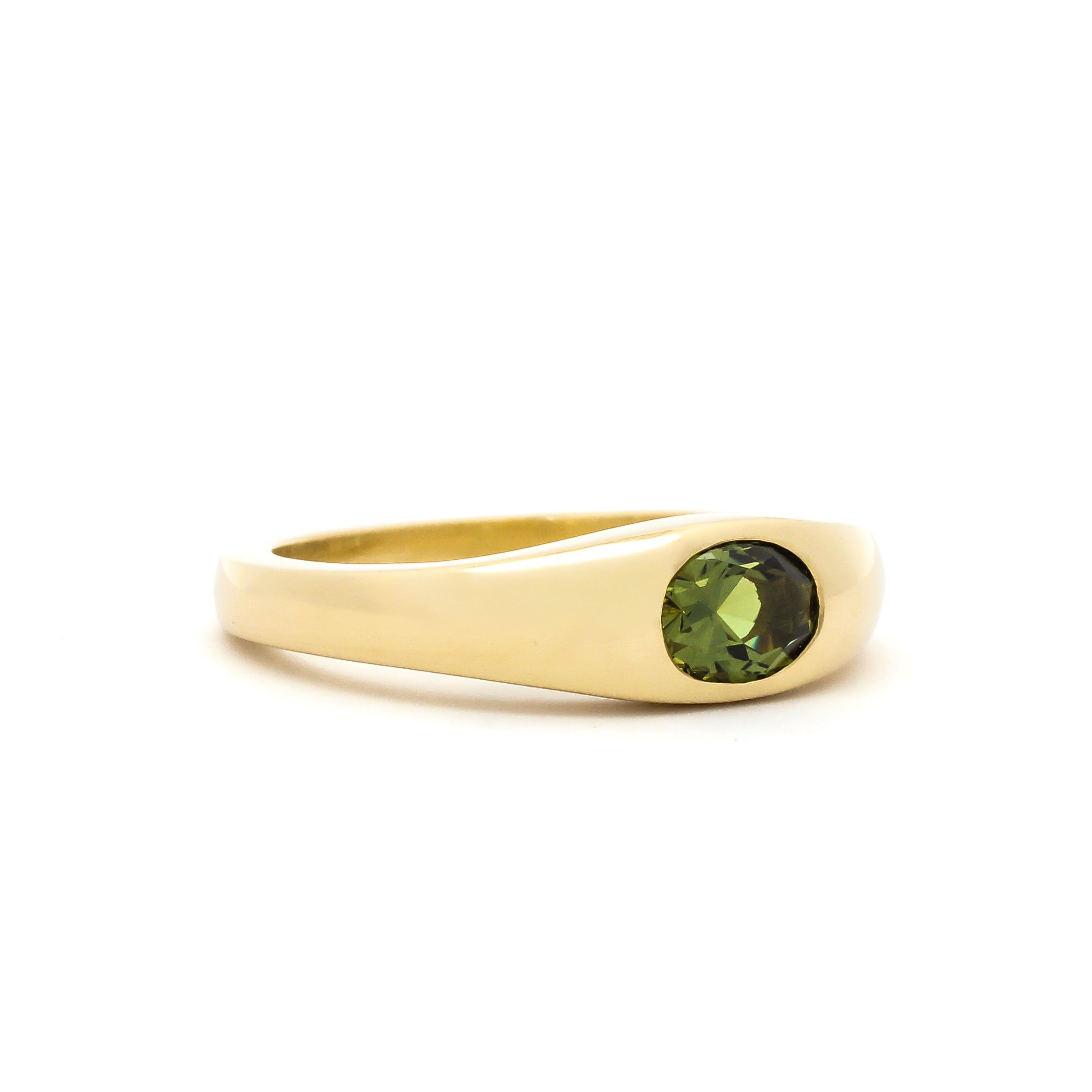 side view of a yellow gold band ring with a bezel set olive green oval sapphire in the centre, against a plain white background