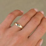 A close-up of a hand wearing a gold ring with a small oval green gemstone, set against a soft beige background.