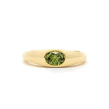 yellow gold band ring with a bezel set olive green oval sapphire in the centre, against a plain white background