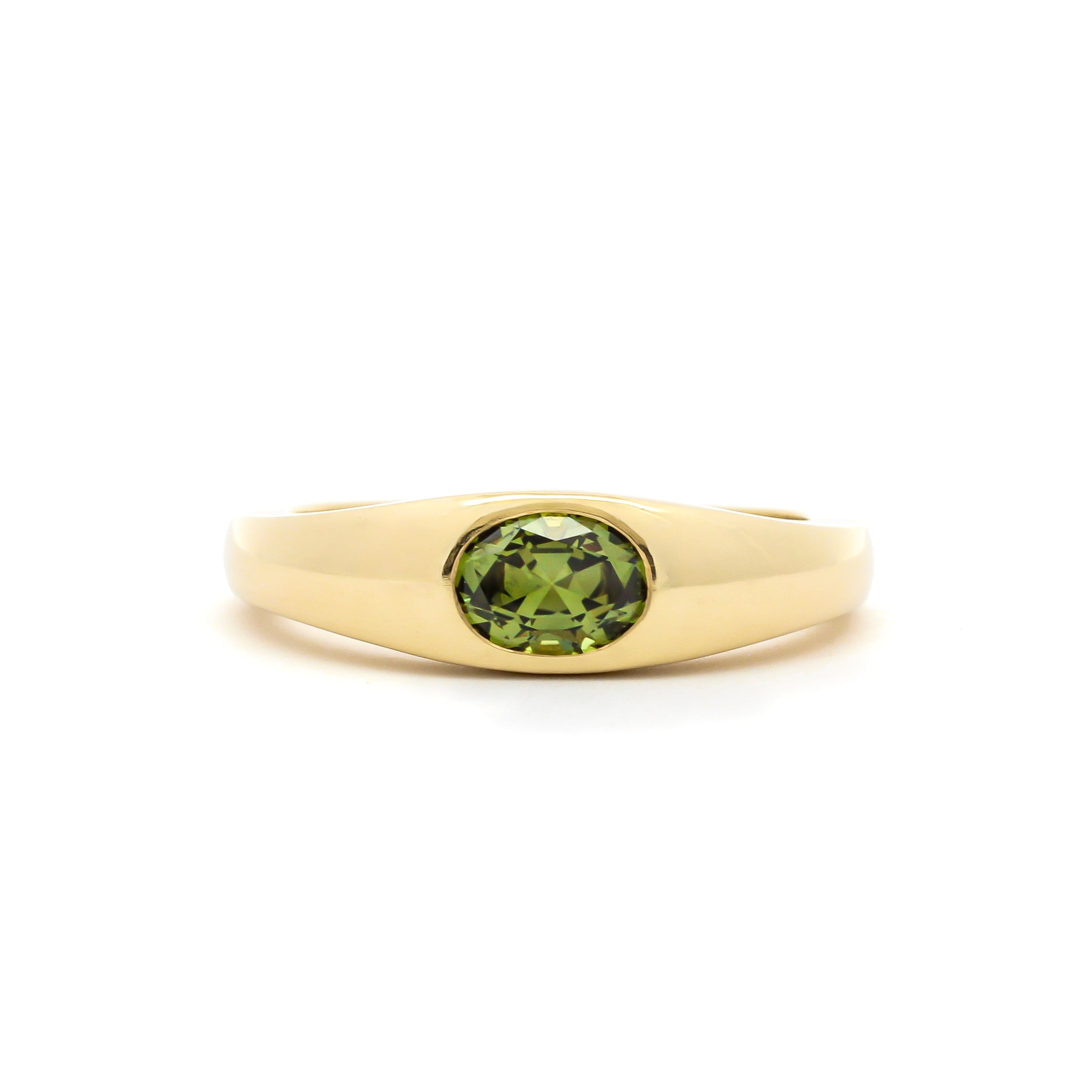 yellow gold band ring with a bezel set olive green oval sapphire in the centre, against a plain white background