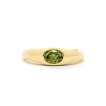 yellow gold band ring with a bezel set olive green oval sapphire in the centre, against a plain white background