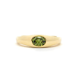 yellow gold band ring with a bezel set olive green oval sapphire in the centre, against a plain white background