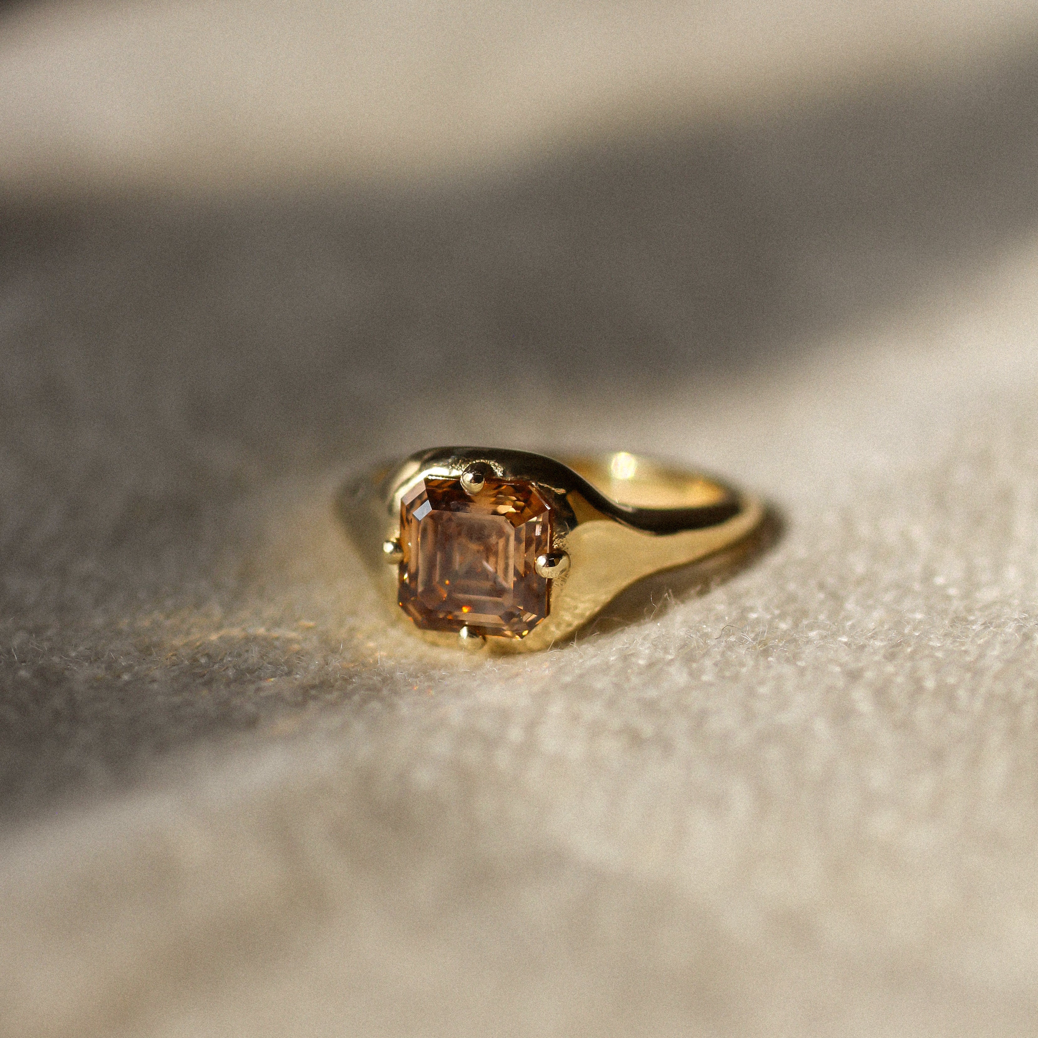 asscher cut brown diamond engagement ring resting on a beige fabric