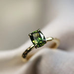 green solitaire engagement ring with blurred background