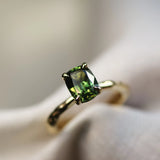 green solitaire engagement ring with blurred background