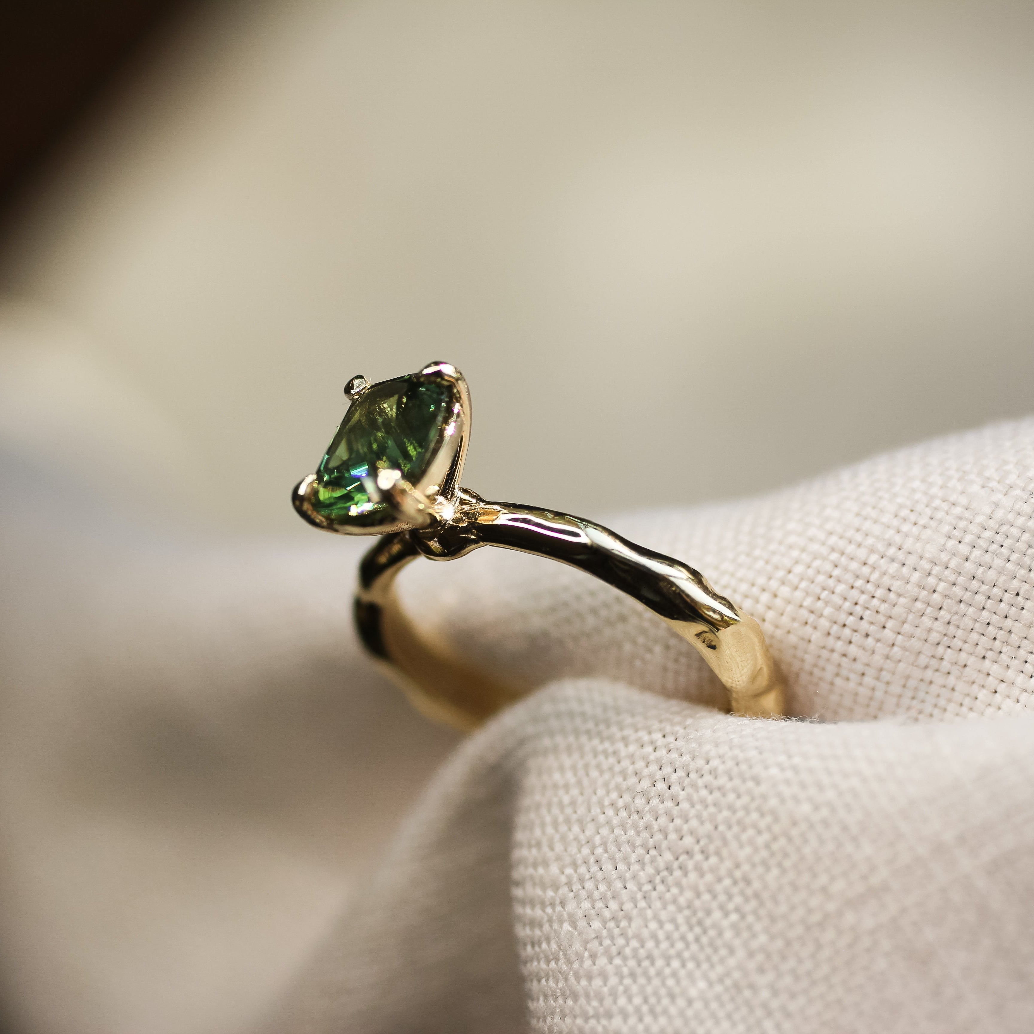 green solitaire sapphire ring with organic textured gold band in neutral fabric