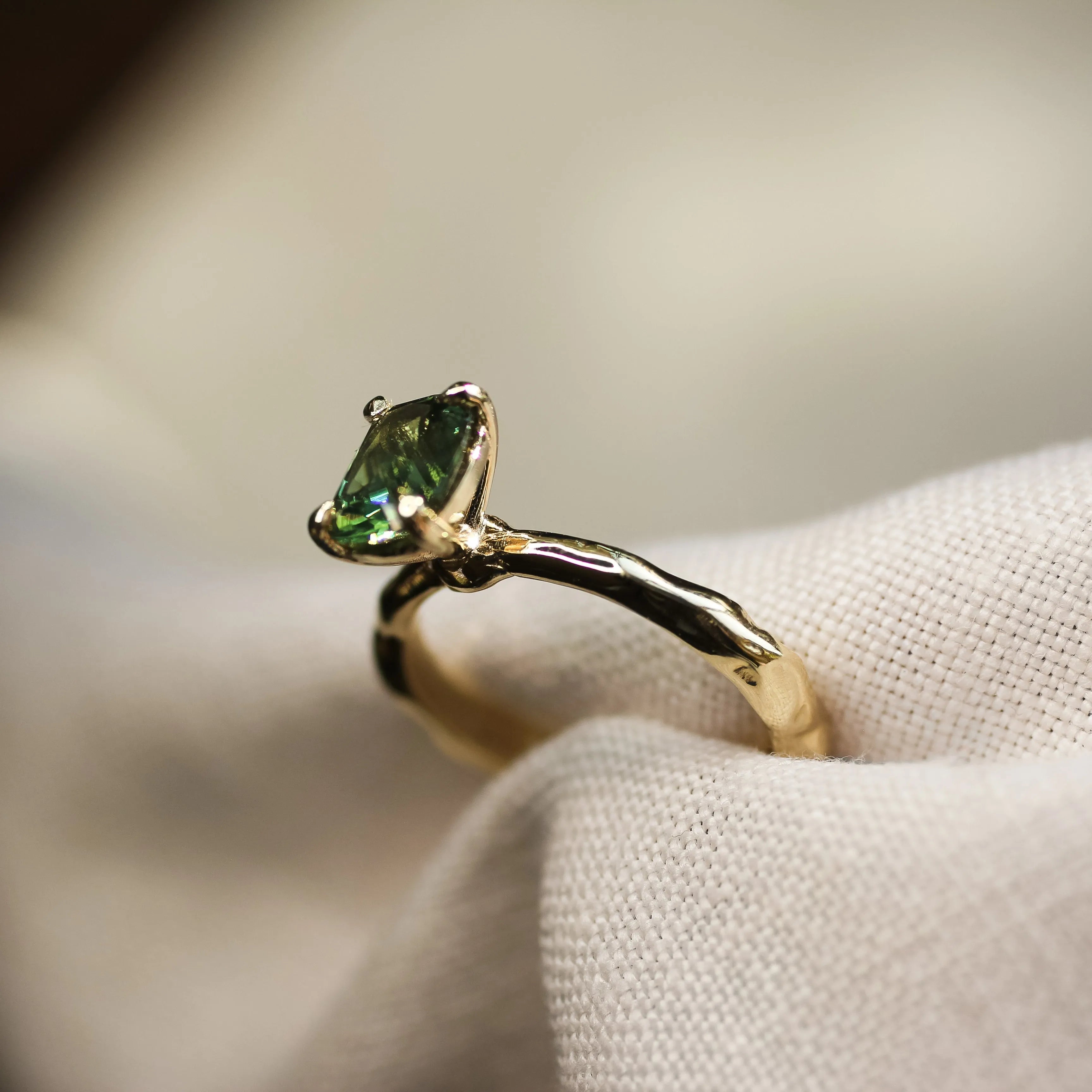 green solitaire sapphire ring with organic textured gold band in neutral fabric