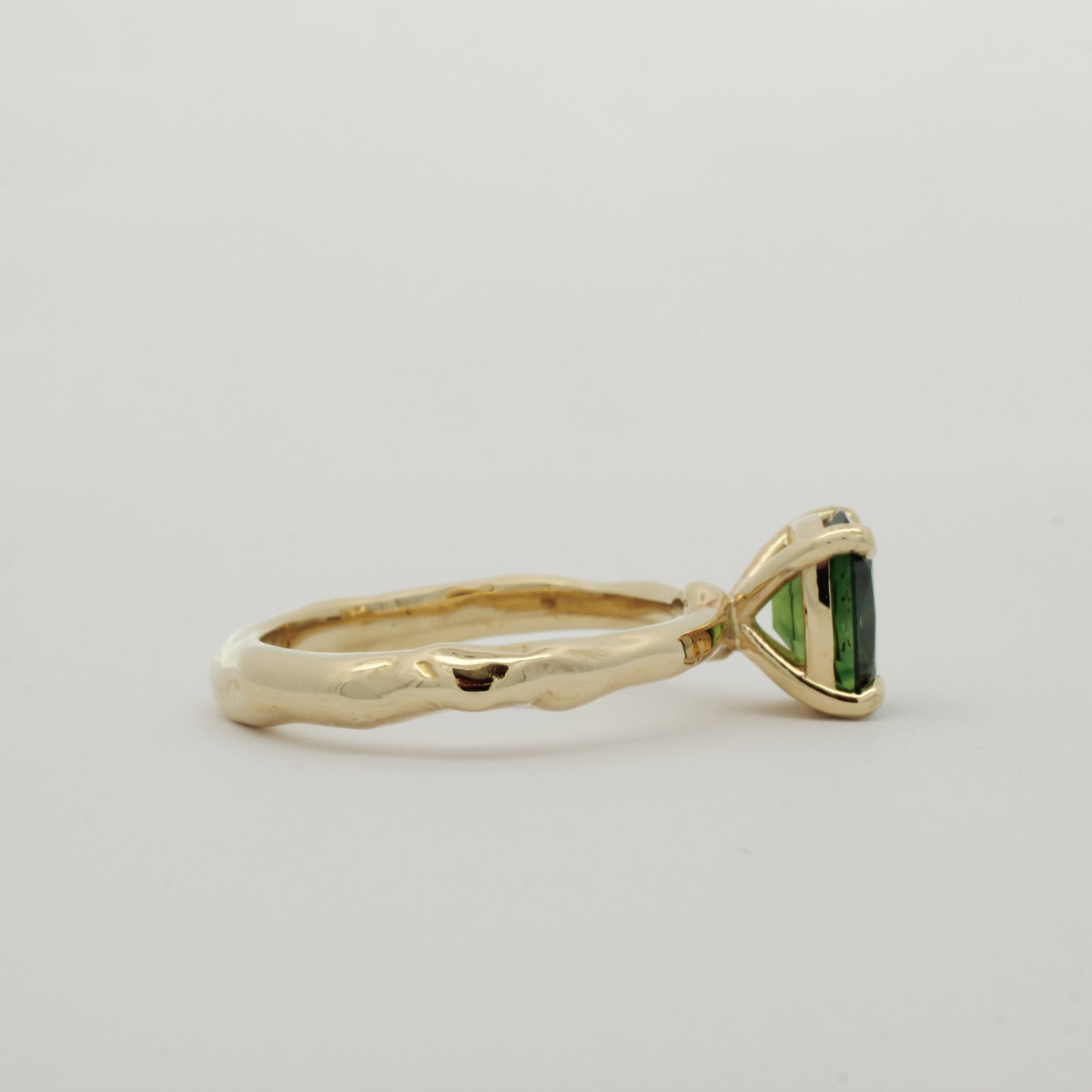 side view of wobbly organic band engagement ring with green sapphire on white background