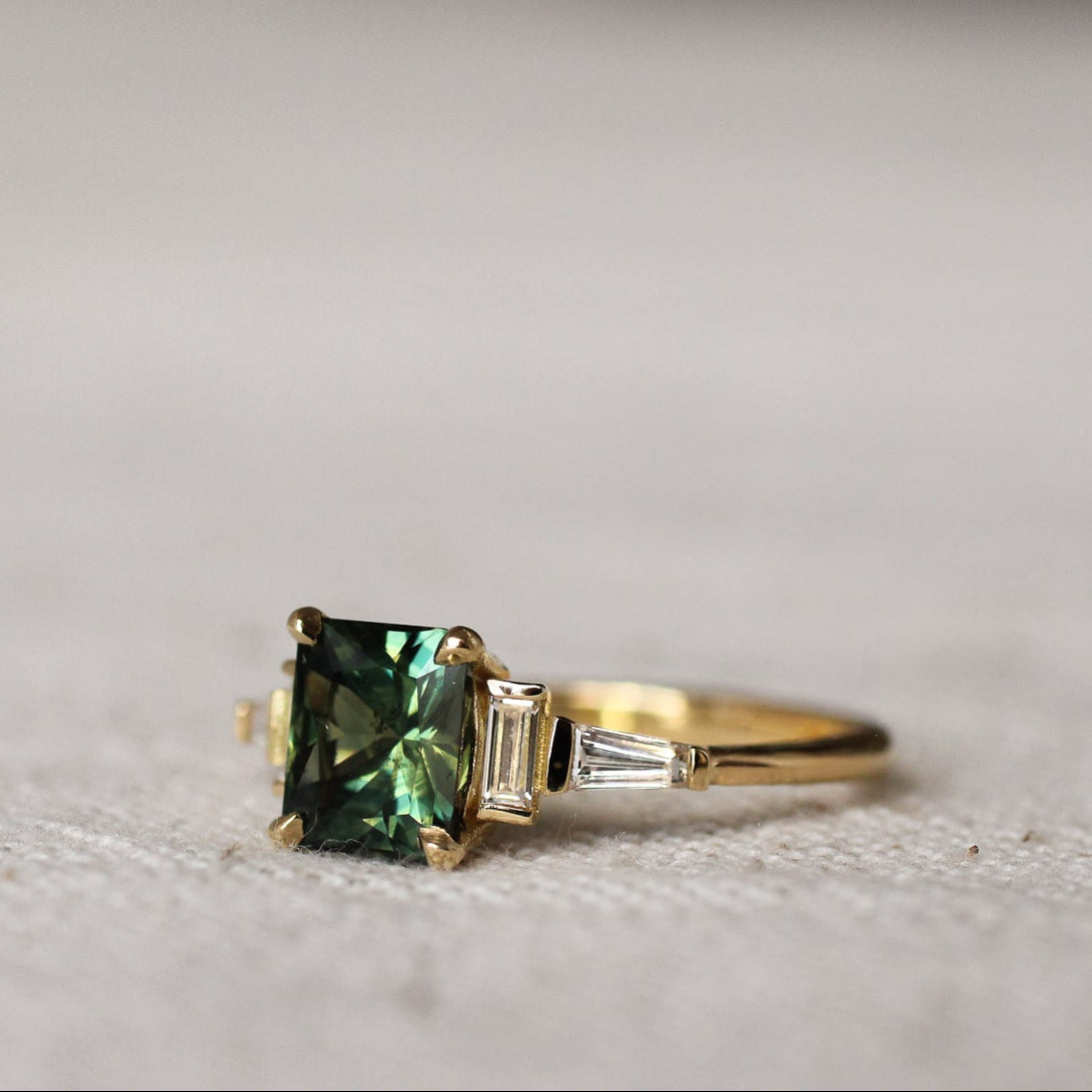 side view of art deco green sapphire and diamond engagement ring on a textured surface