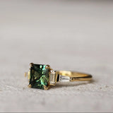 side view of art deco green sapphire and diamond engagement ring on a textured surface