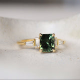 Art deco style engagement ring with a green gemstone and baguette cut diamonds on a white surface