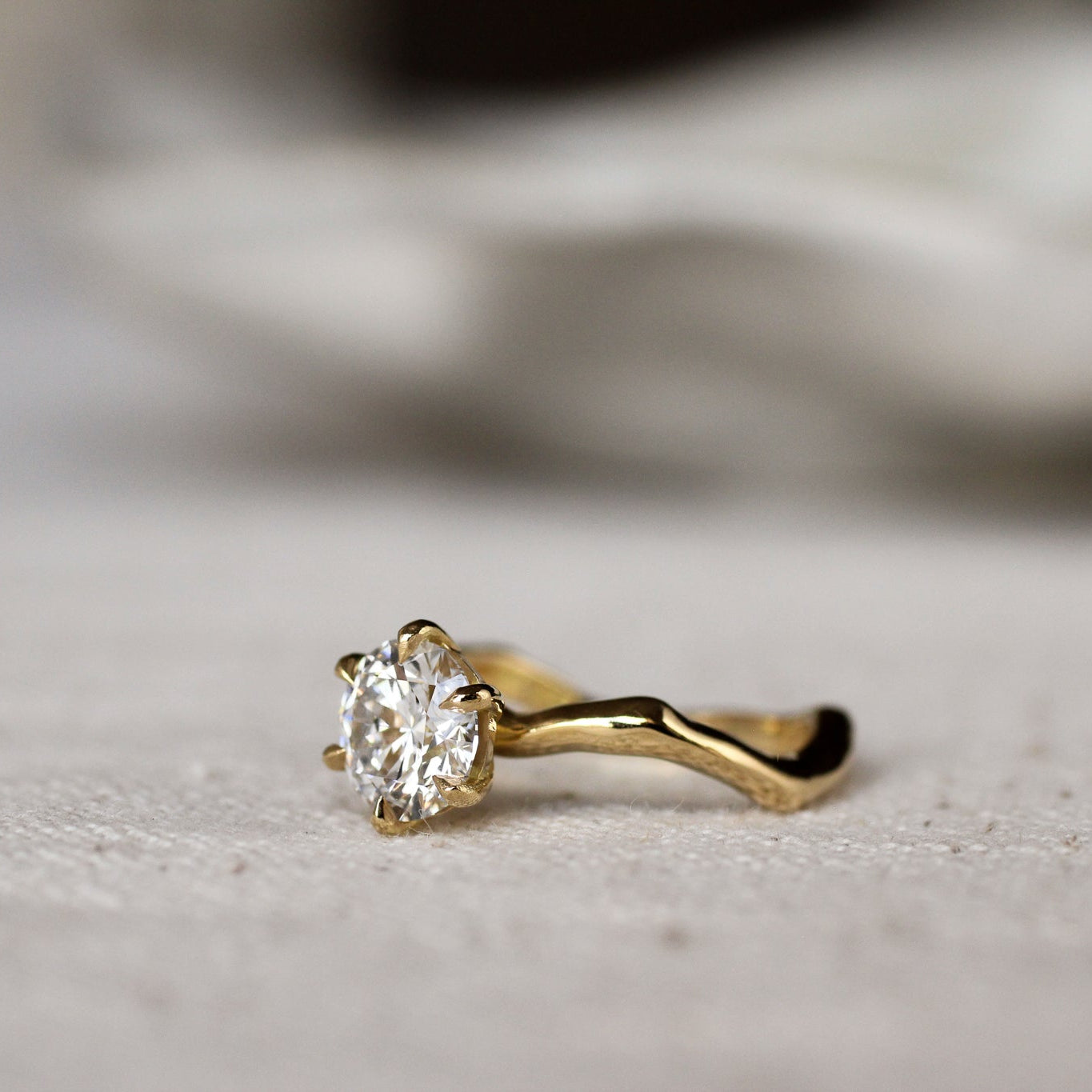 Gold ring with a round diamond and waved organic-textired band on a light gray surface