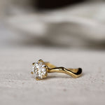 Gold ring with a round diamond and waved organic-textired band on a light gray surface