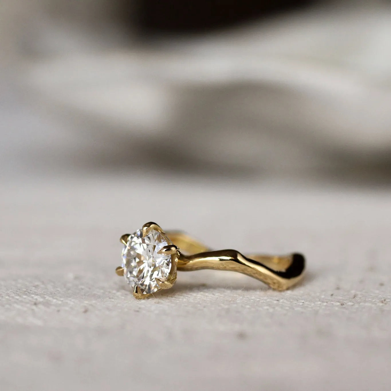 Gold ring with a round diamond and waved organic-textired band on a light gray surface