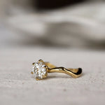 Gold ring with a round diamond and waved organic-textired band on a light gray surface