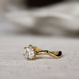 Gold ring with a round diamond and waved organic-textired band on a light gray surface