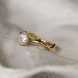 Gold ring with a diamond and organic wavy shank on a textured fabric background