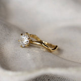 Gold ring with a diamond and organic wavy shank on a textured fabric background