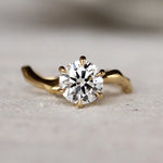 Gold ring with a diamond and wavy organic band on a light surface