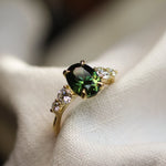 ring with large oval green sapphire and round diamonds in blurred white fabric 