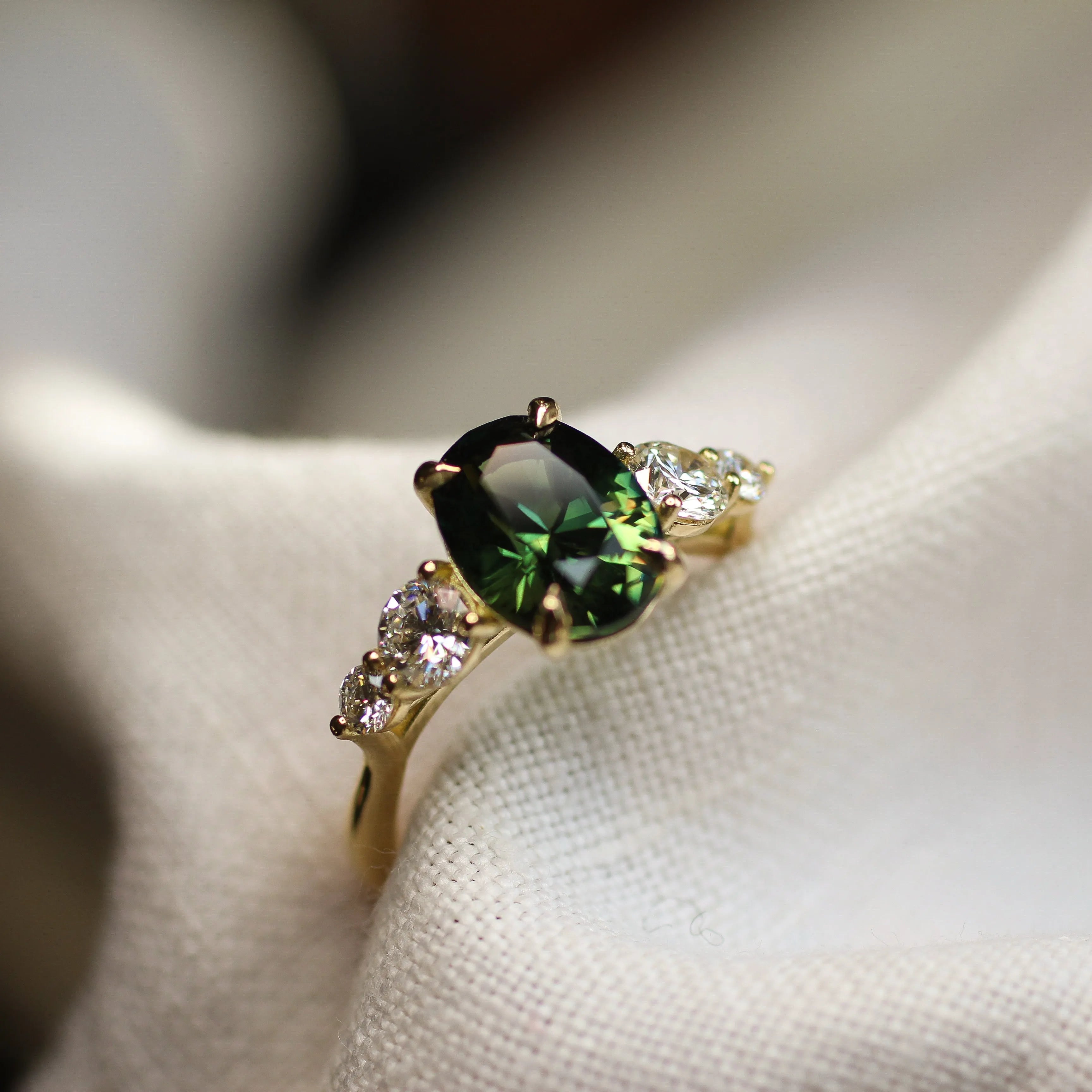 ring with large oval green sapphire and round diamonds in blurred white fabric 