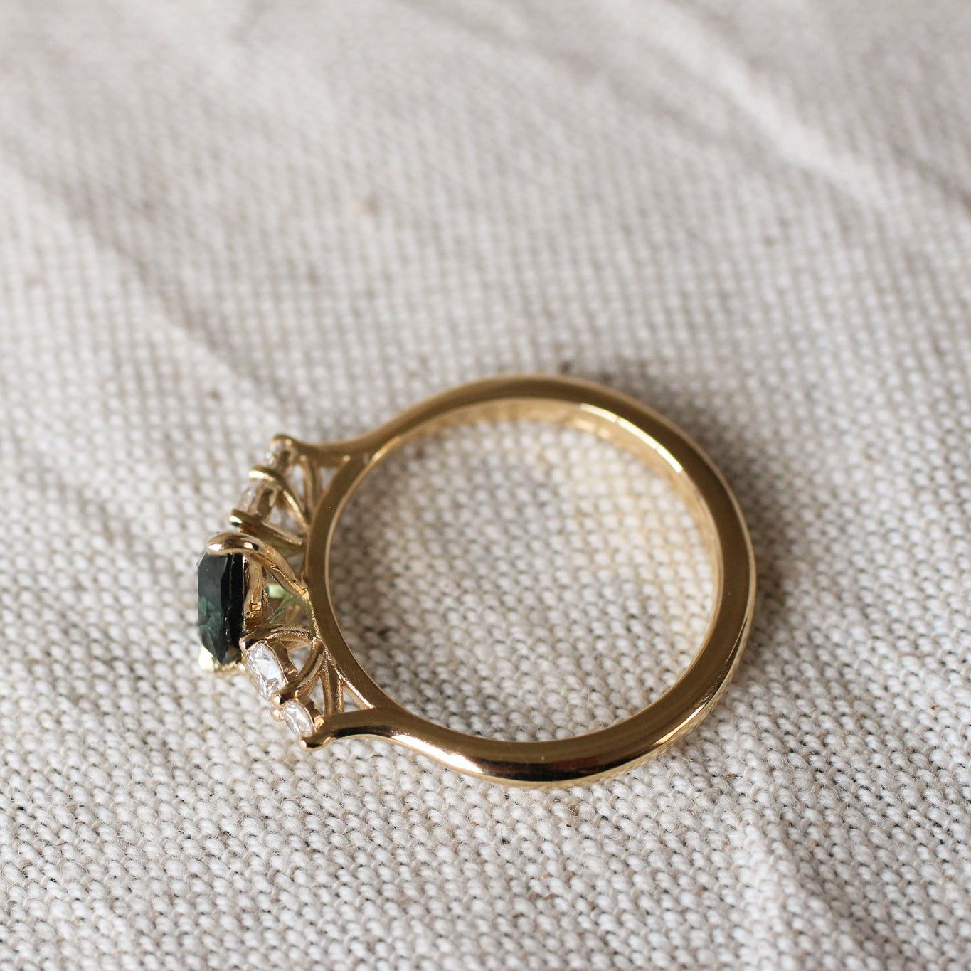 top view displaying high-set collet of pear sapphire and diamond engagement ring on a beige fabric